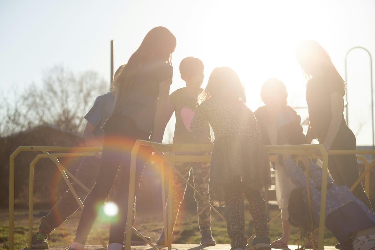 Photo of children on a playground merry-go-round silhouetted by the sun