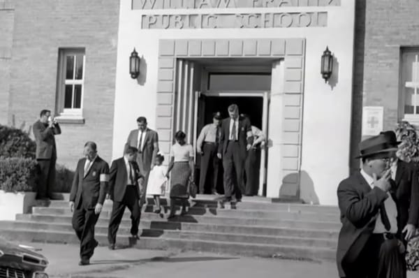 Photo of Ruby Bridges walking out of school, holding her mother's hand, surrounded by marshals
