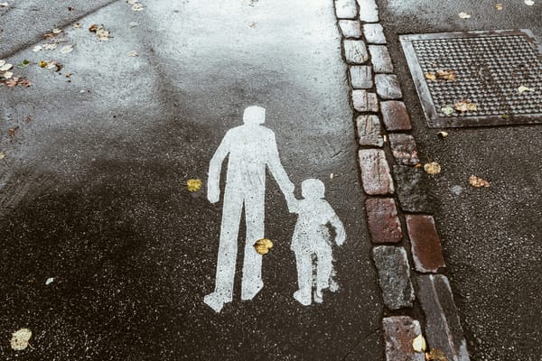 Photo of a painted crosswalk sign, depicting an adult and a child holding hands, on wet pavement