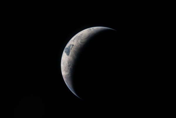 A NASA photo of Earth in shadow, taken from Artemis II. Only a crescent of Earth is visible amidst darknes.